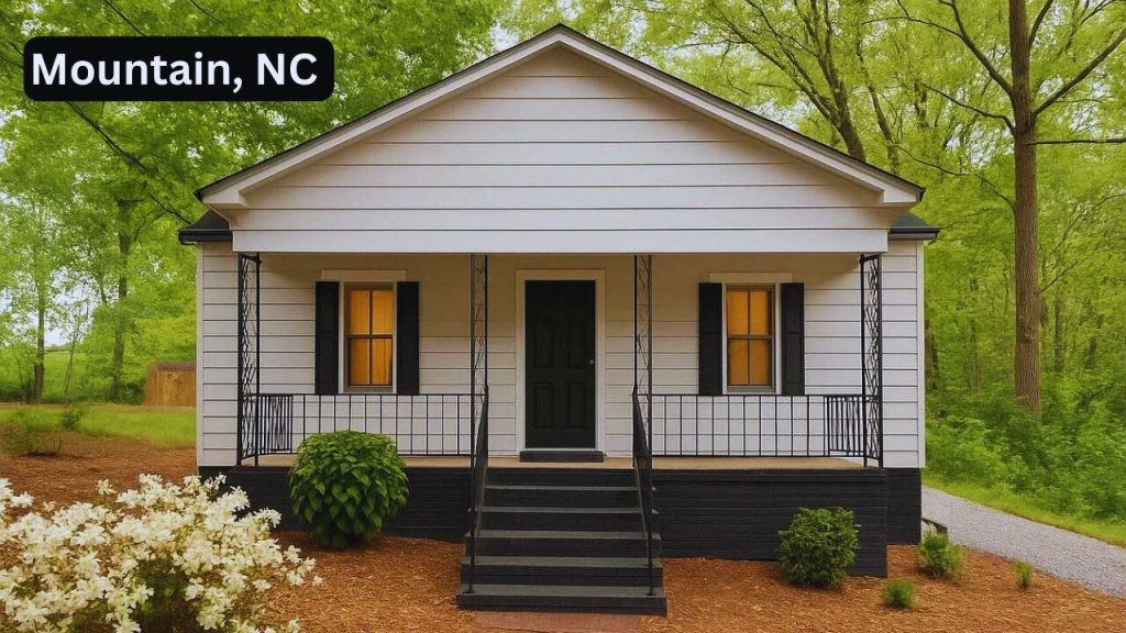 Cozy white cottage with green door and porch set in a wooded area.