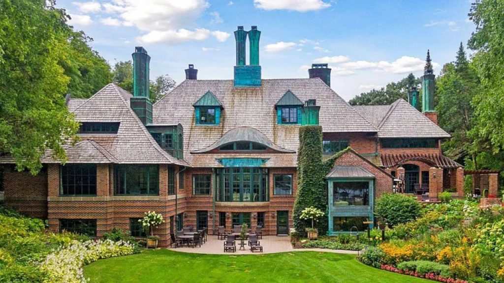 A beautiful colonial modern home with brick walls, green patina chimneys, and a lush garden patio, nestled among trees.