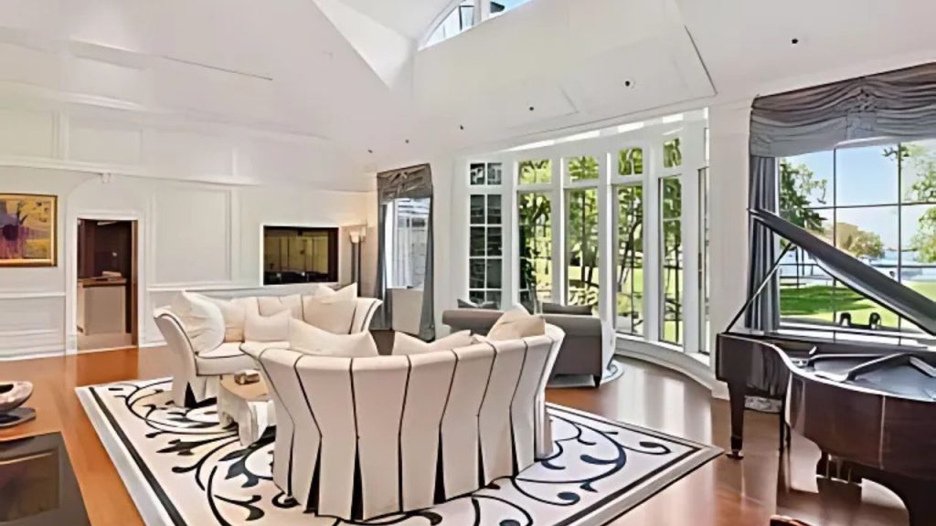 A bright living room with large windows, a grand piano, and cozy seating, overlooking a lush lake view.