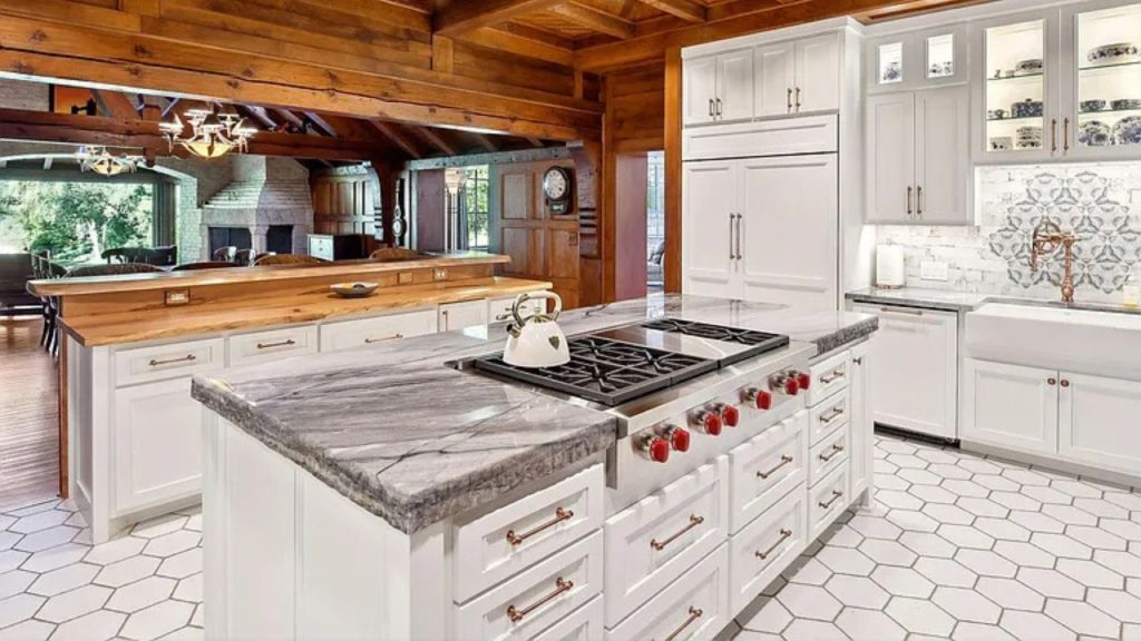 A rustic kitchen with wooden beams, a marble island, and glass cabinets, opening to a cozy living area.
