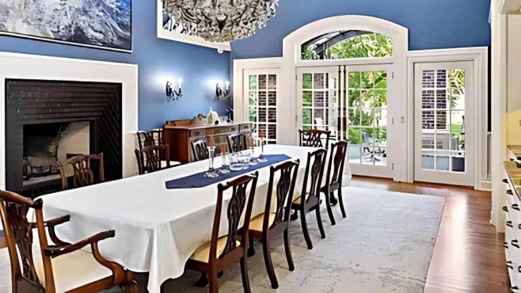 A cozy dining room with blue walls, a chandelier, and French doors opening to a garden view.