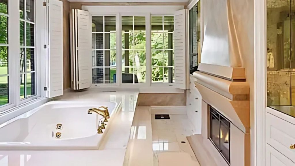 A peaceful bathroom with a soaking tub, fireplace, and large windows overlooking greenery.