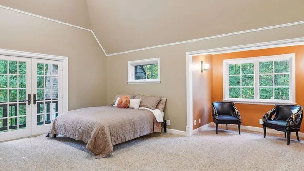 A cozy bedroom with a bed, French doors, and black chairs against an orange accent wall.