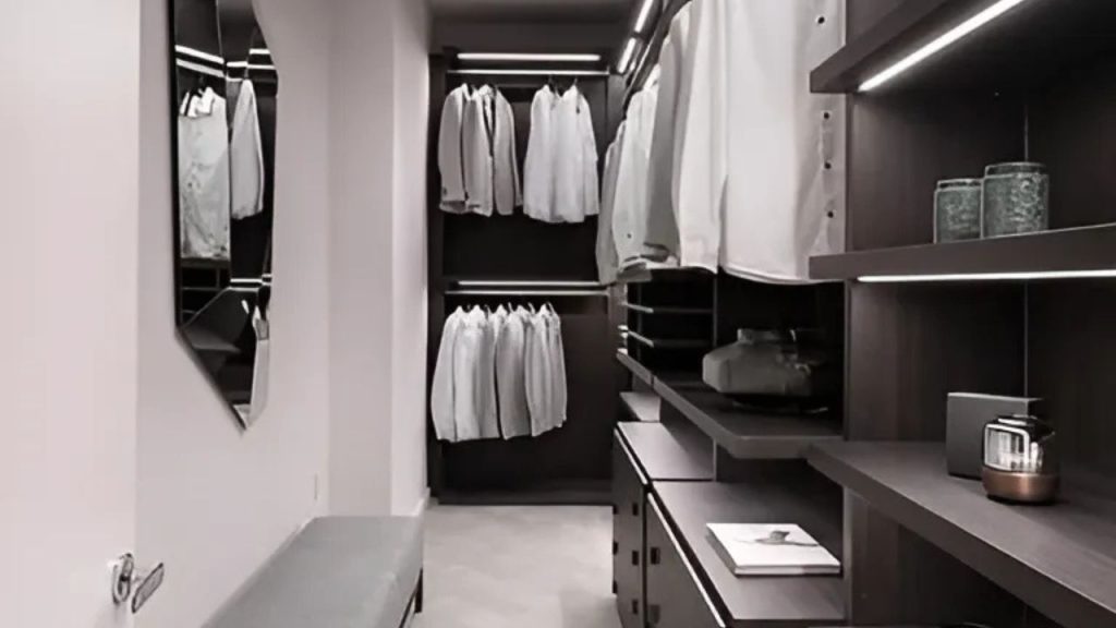 A stylish walk-in closet with white shirts, LED lighting, and a modern bench and mirror.