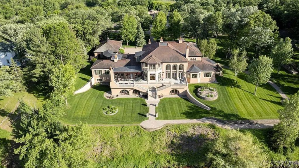An aerial view of a luxurious beige mansion with a balcony and lush gardens on a large lot in Perham, MN.