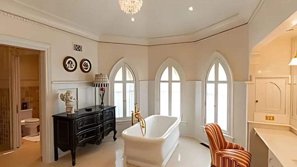 A peaceful bathroom with a white tub, chandelier, and arched windows.
