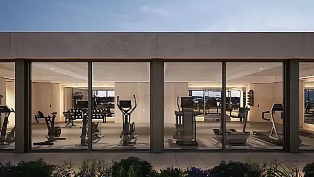 Glass-walled rooftop gym with workout machines and city views.