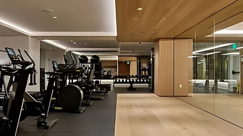 A modern home gym with cardio machines, wooden ceilings, mirrors, and soft lighting.