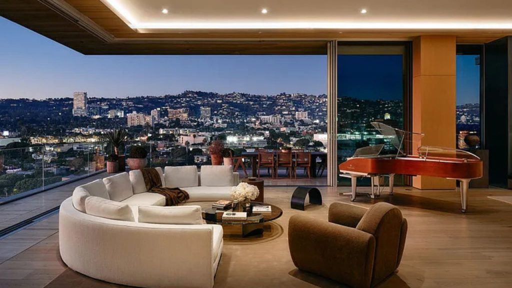 A luxurious living area with a curved white sofa, red piano, and stunning city skyline view through large windows.