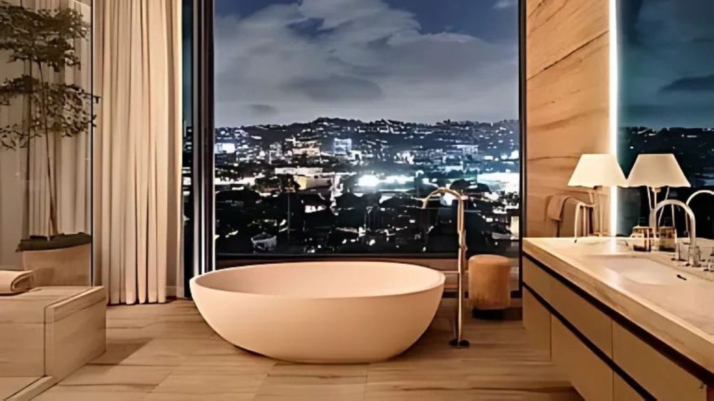 A luxurious bathroom with a freestanding tub, city skyline view, and elegant lighting.
