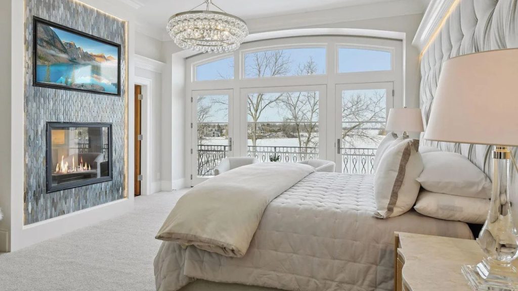A luxurious bedroom with a fireplace, chandelier, and large windows.