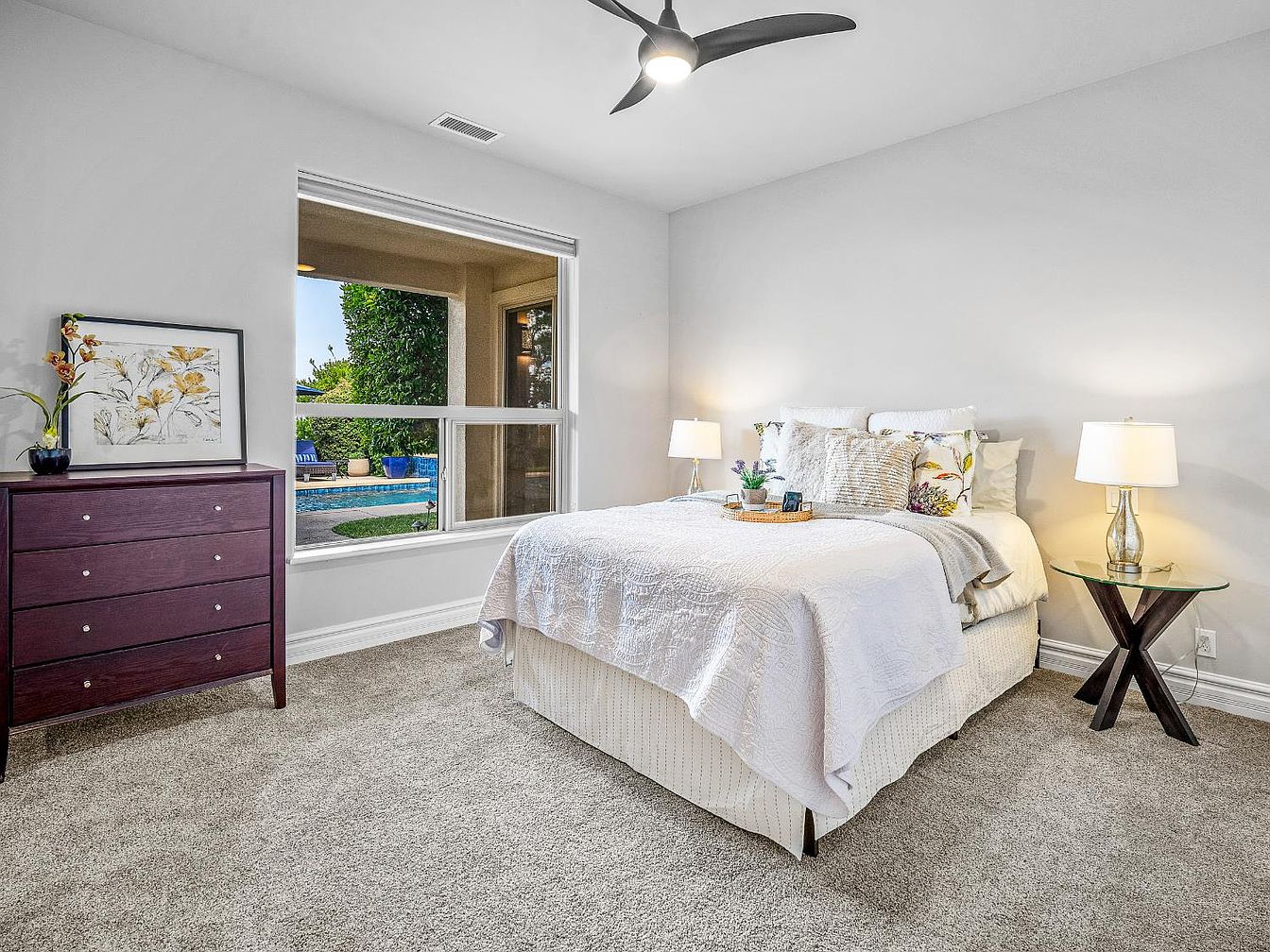 Guest bedroom with white bedding, wooden dresser, and large window