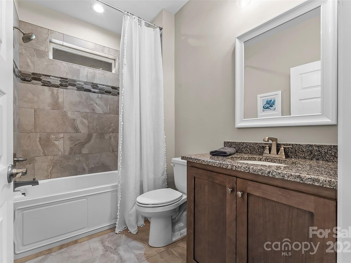 Bathroom vanity with granite countertop next to tub and tiled shower with white curtain