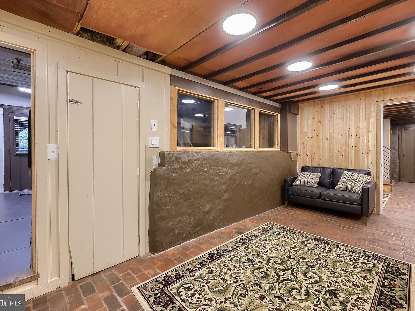 Cozy basement sitting area with exposed ceiling beams and brick flooring.
