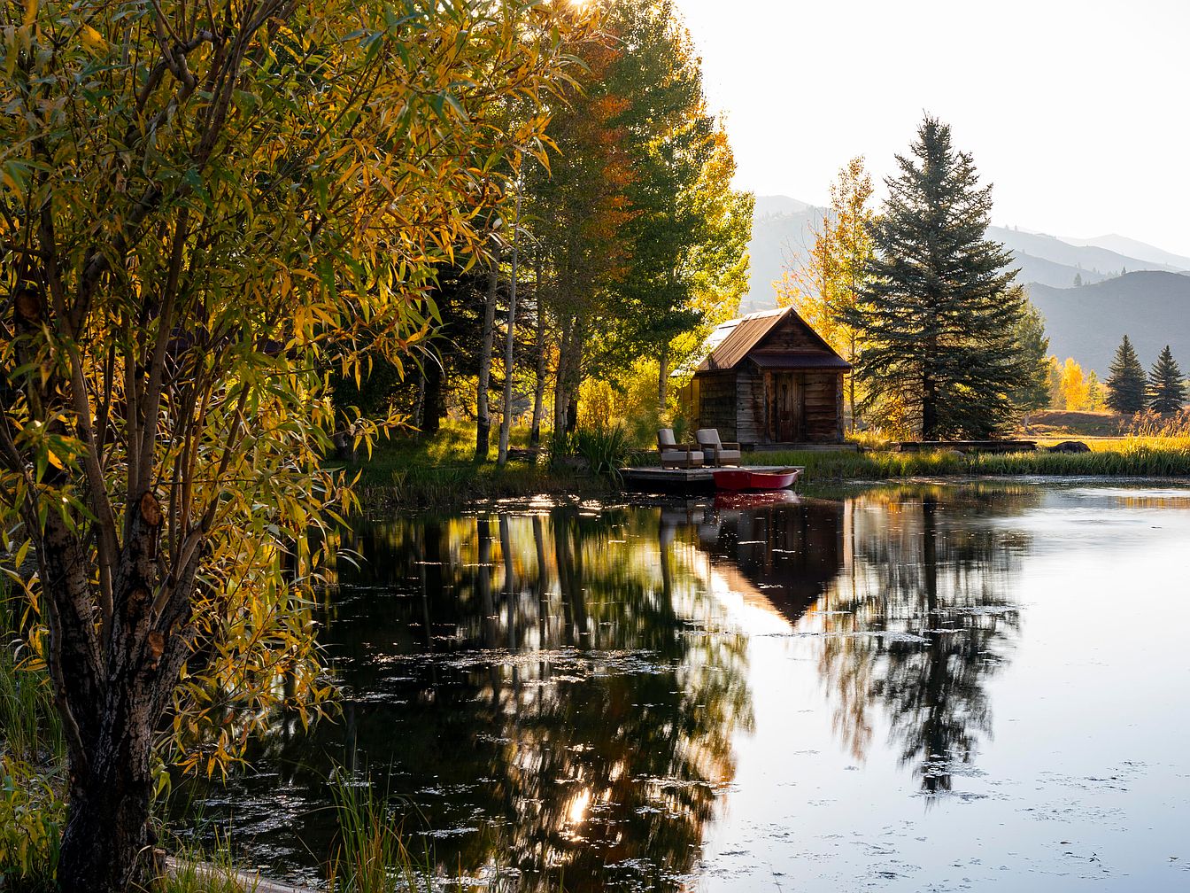 Peaceful pond with a small wooden cabin and dock with chairs
